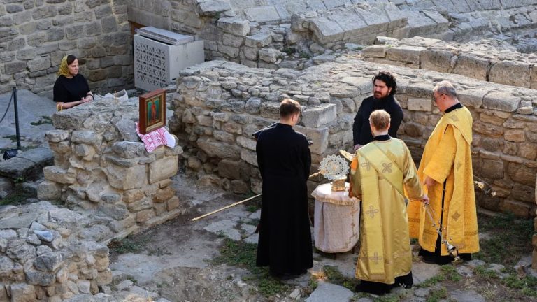 Priests conduct a religious ceremony at historical stone ruins outdoors.