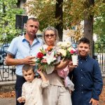 A family of four standing together in a park with a large flower bouquet