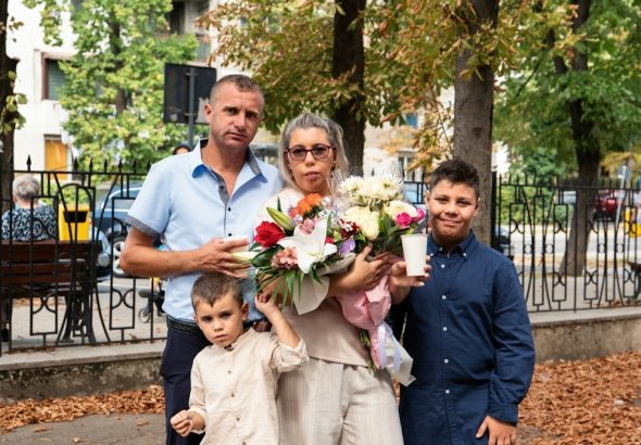 A family of four standing together in a park with a large flower bouquet