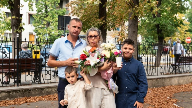 A family of four standing together in a park with a large flower bouquet